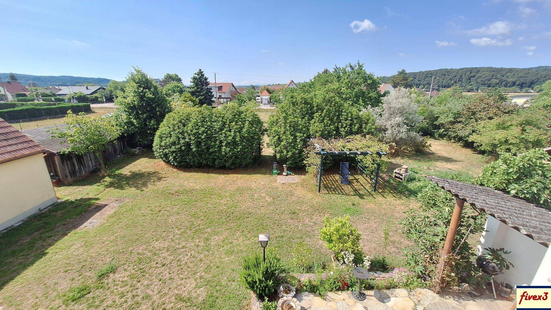 Großer Garten mit Rasenfläche, Bäumen und einer kleinen Pergola, umgeben von ländlicher Bebauung.