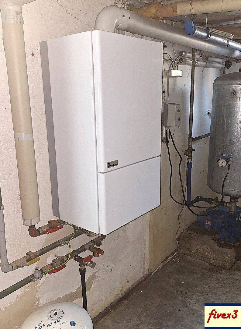 Kellerraum mit wandmontiertem Heizkessel und komplexen Rohrleitungen an der Wand.