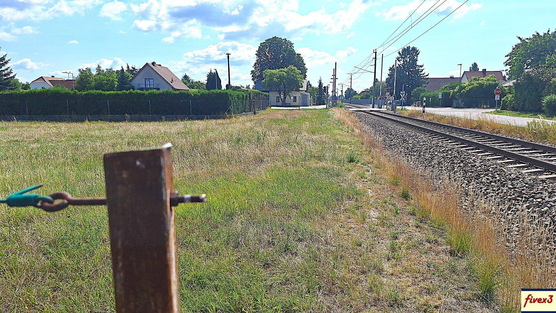 Blick auf eine Bahntrasse, die an einem Grüngürtel vorbeiführt, mit Häusern im Hintergrund.