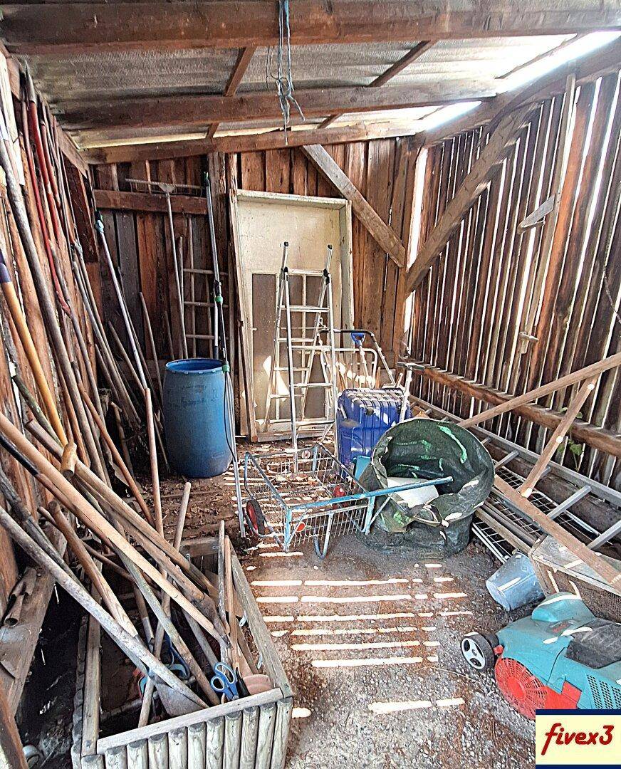 Innenansicht eines Holzschuppens, gefüllt mit Gartengeräten, Leitern und verschiedenen Gegenständen.