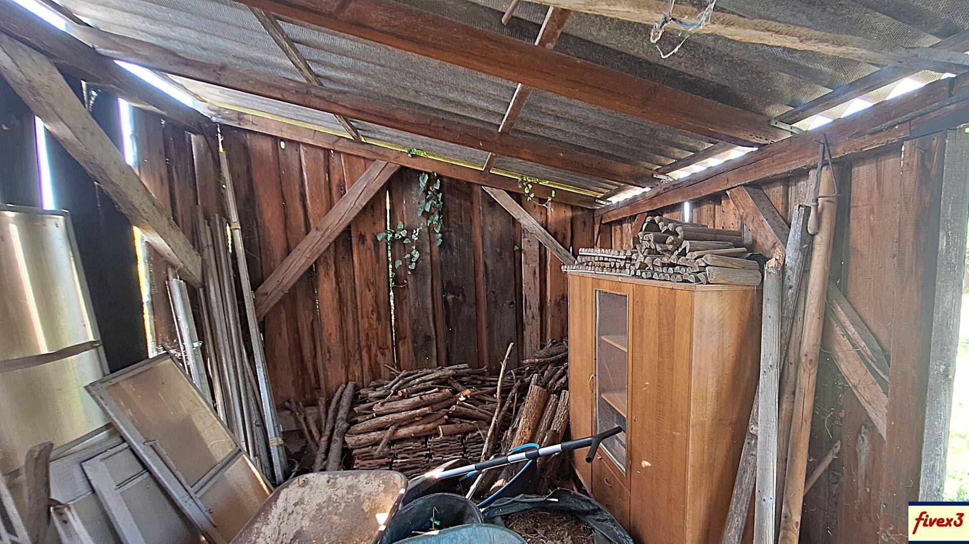 Innenansicht eines Holzschuppens mit gelagertem Holz, Werkzeugen und einem kleinen Schrank.