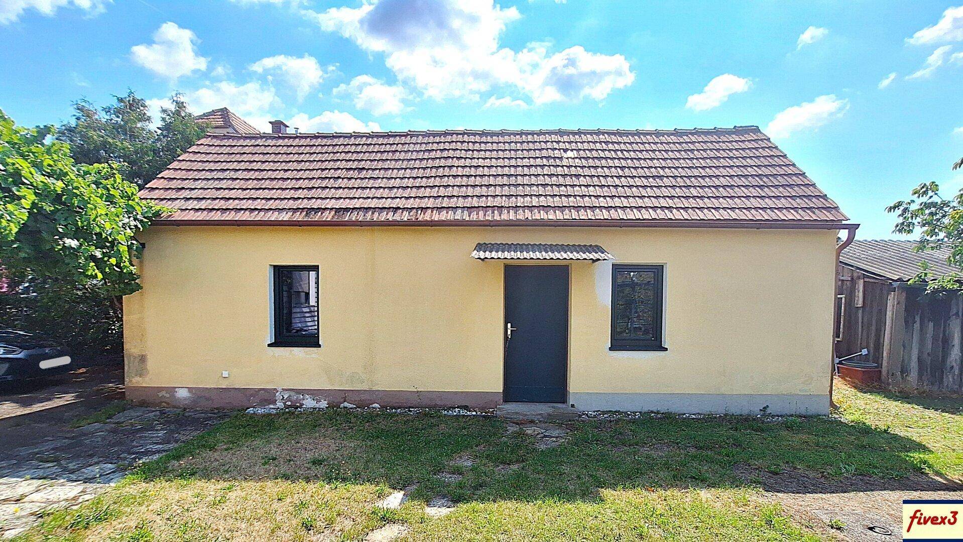 Vorderansicht eines einfachen, einstöckigen Hauses mit gelber Fassade und Ziegeldach.