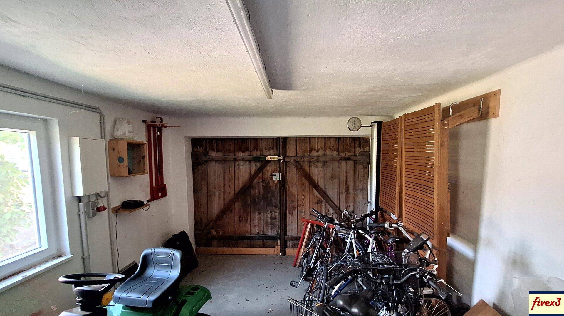Eine Garage mit Holztüren, Fahrrädern und einem Rasenmäher, die als Abstellraum dient.