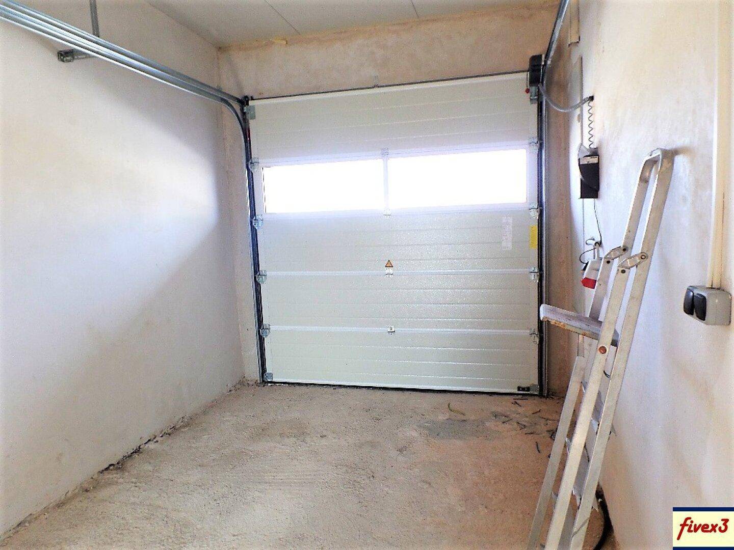 Innenansicht einer Garage mit geschlossenem Sektionaltor, einem robusten Betonboden und einer Leiter an der Wand.