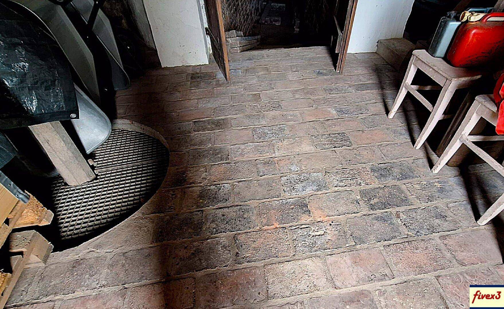 Rustikaler Ziegelboden in einem Kellerraum, der zu einem weiteren Gewölbe führt, mit alten Möbeln.