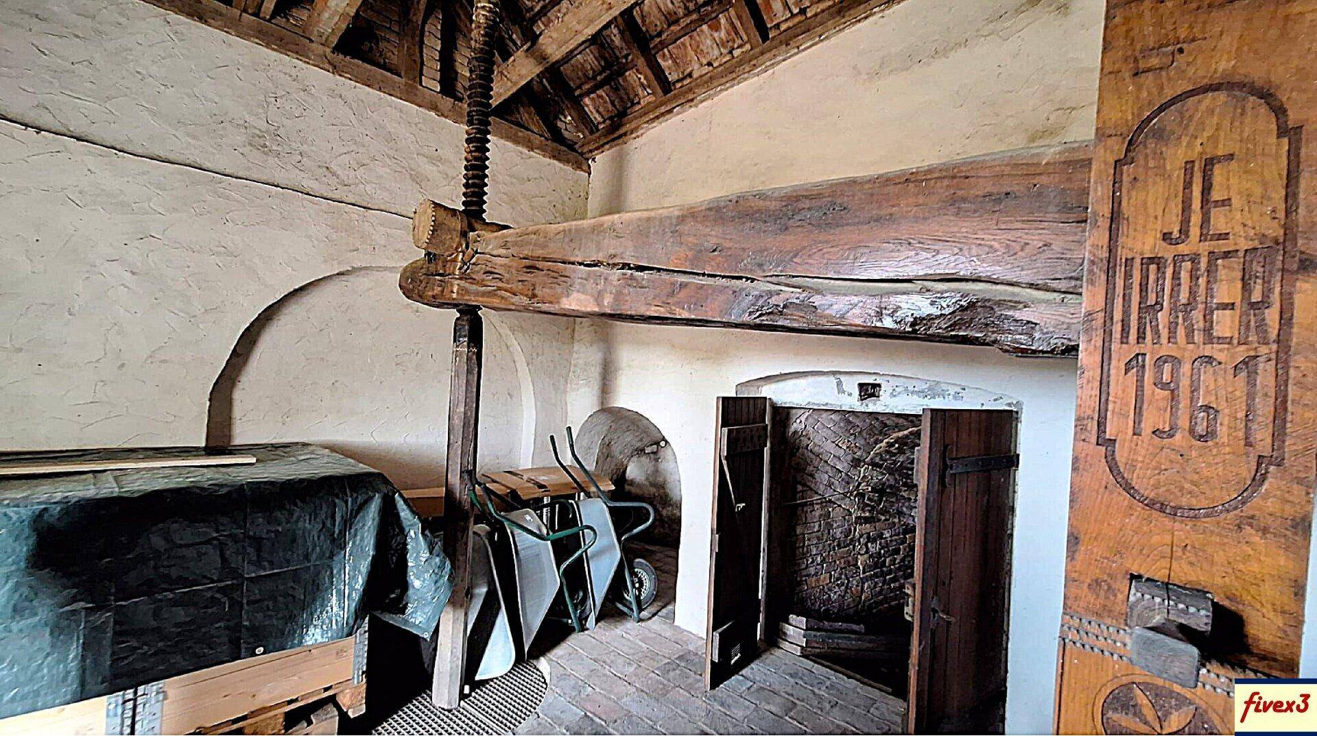 Detailansicht eines alten Weinkellers mit Holzbalken, Ziegelboden und einer historischen Holzpresse.