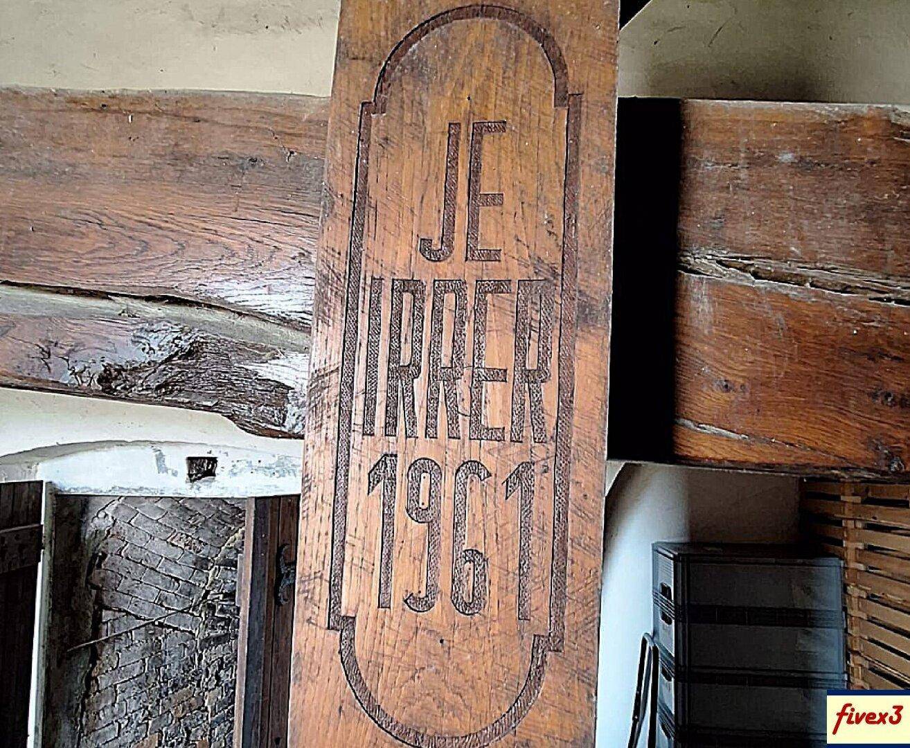 Detailansicht eines massiven Holzbalkens mit einer eingravierten Jahreszahl 1961 und Initialen.