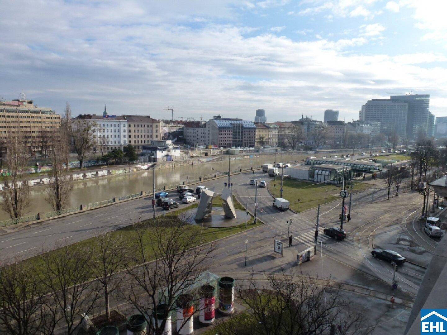 Panoramablick über eine belebte Stadtstraße mit Fluss und urbaner Bebauung.