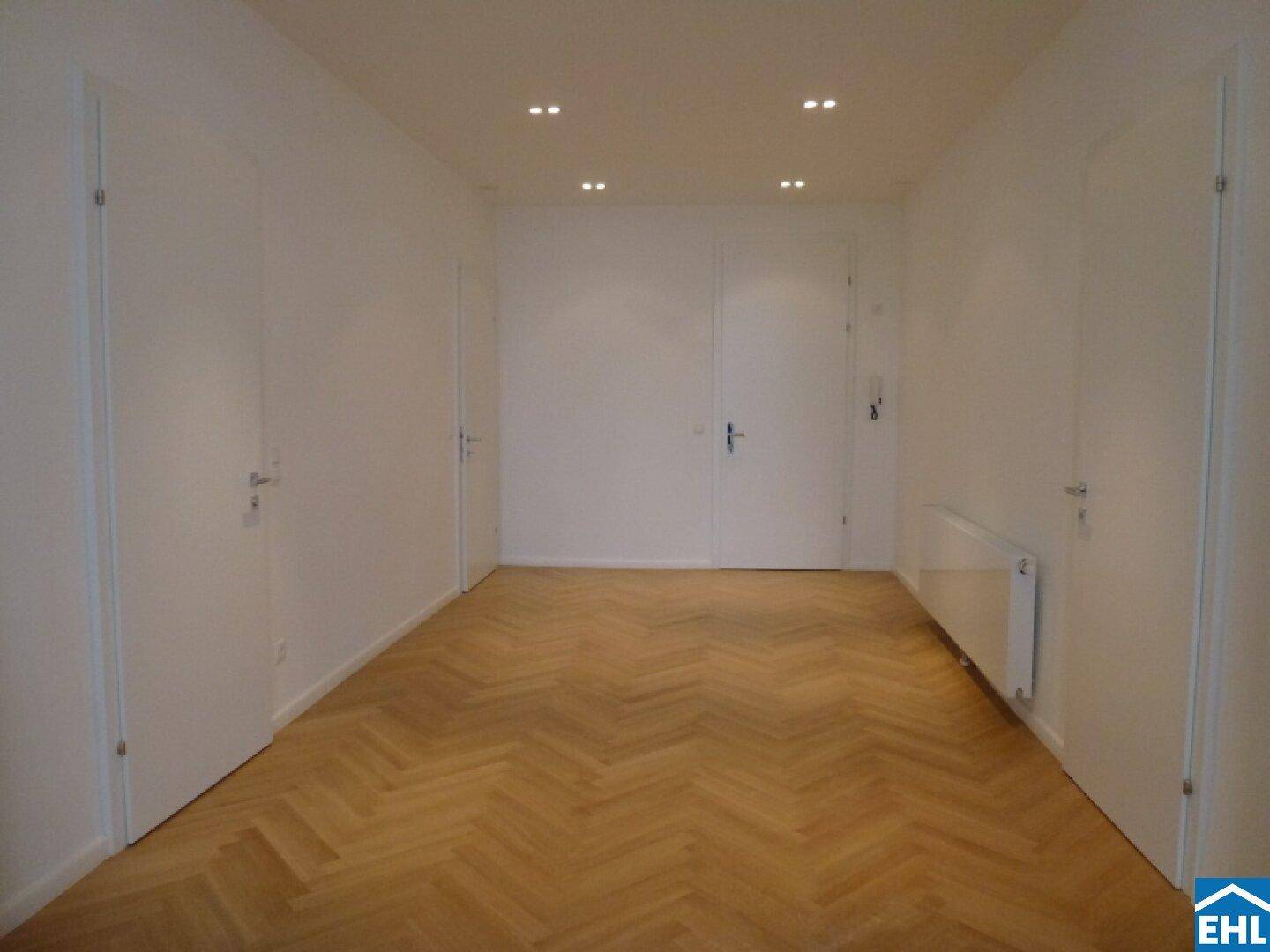 Heller Flur mit Fischgrätparkett, mehreren Türen und integrierter Deckenbeleuchtung.