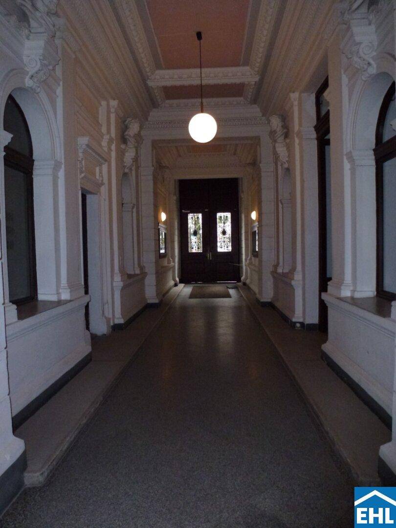 Prunkvoller Eingangsbereich eines Altbaus mit Säulen, Stuckdecke und langer Passage.