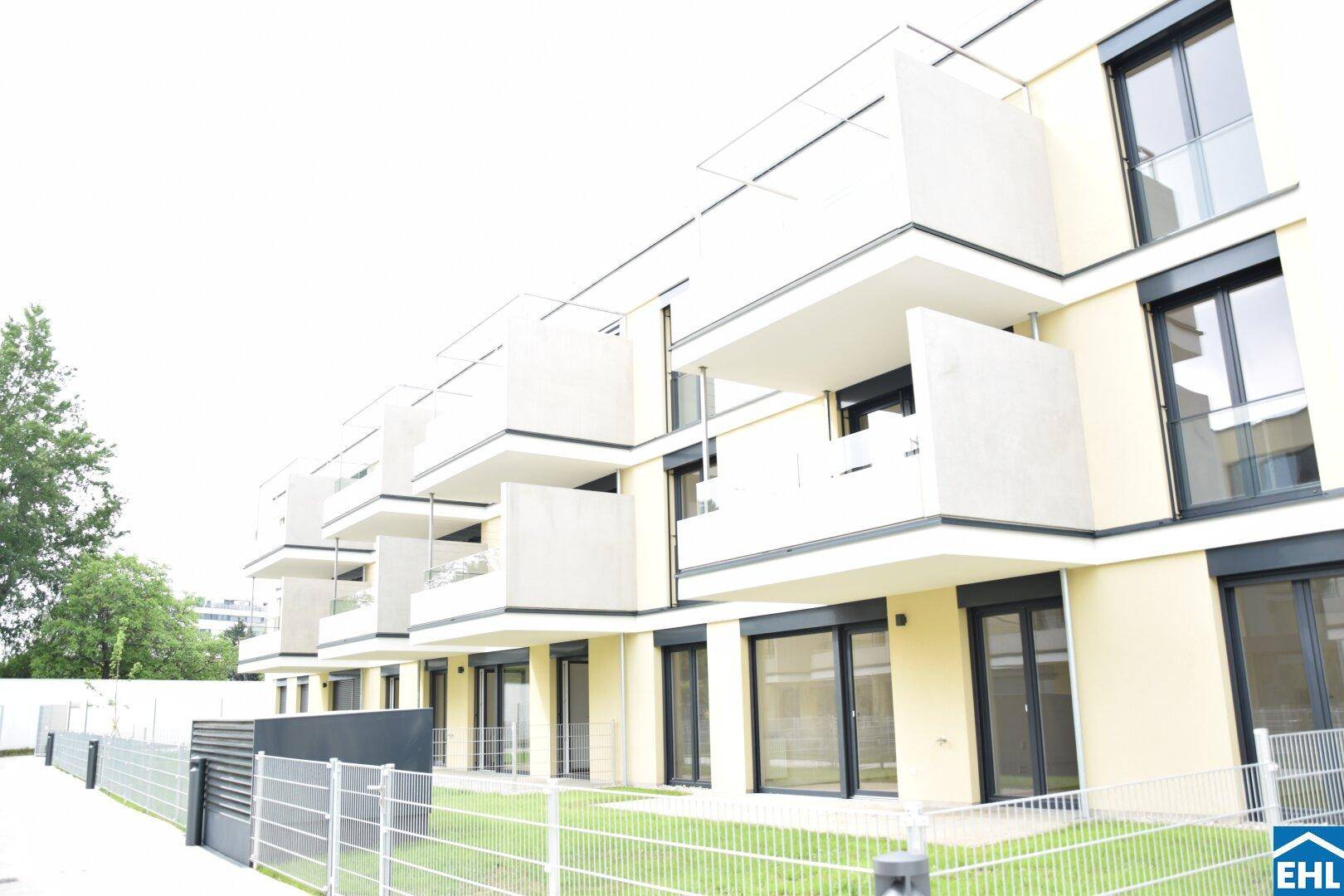 Moderne Wohnanlage mit hellgelber Fassade, Balkonen und privaten Gartenbereichen im Erdgeschoss.