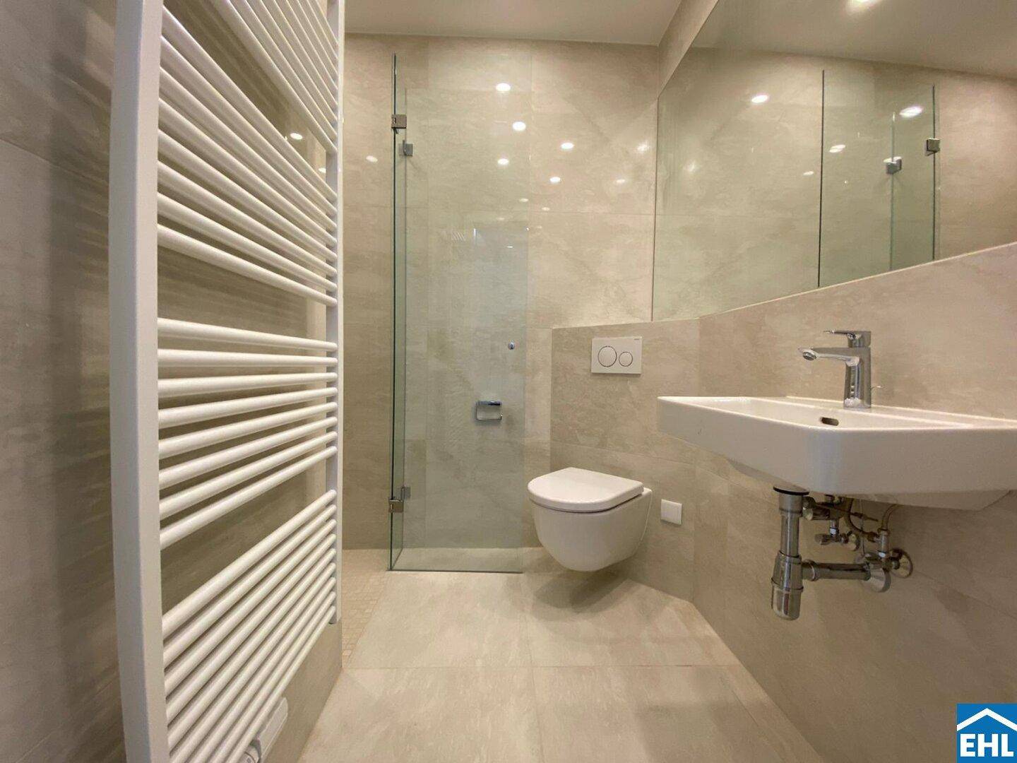 Elegantes Badezimmer mit beigefarbenen Fliesen, wandhängendem WC, Einzelwaschbecken und Duschbereich.