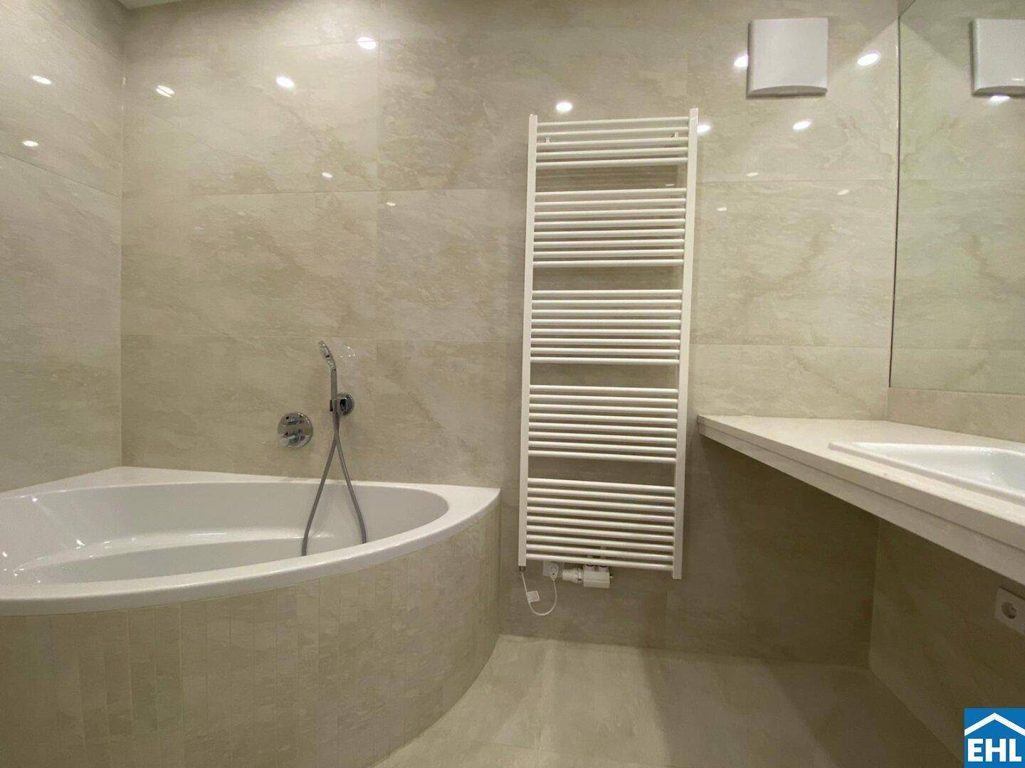 Geräumiges Badezimmer mit beigefarbenen Fliesen, einer Eckbadewanne und einem beheizten Handtuchhalter.