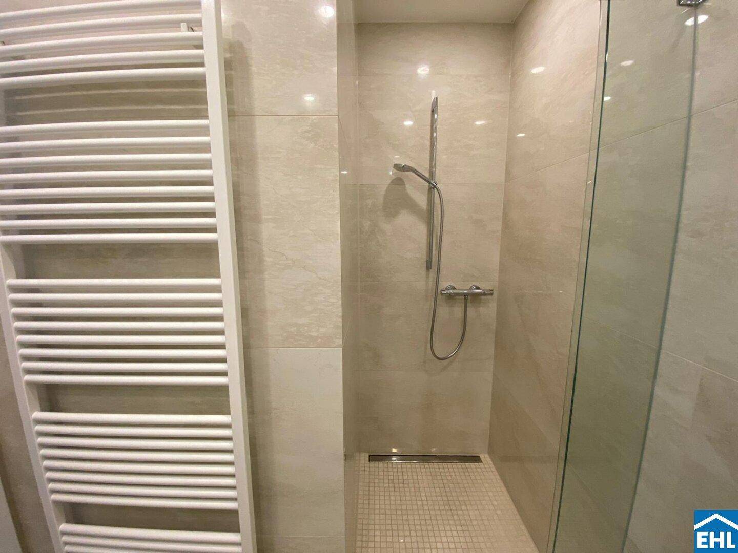 Modernes Badezimmer mit beigefarbenen Fliesen und einer ebenerdigen Dusche mit Glasabtrennung.