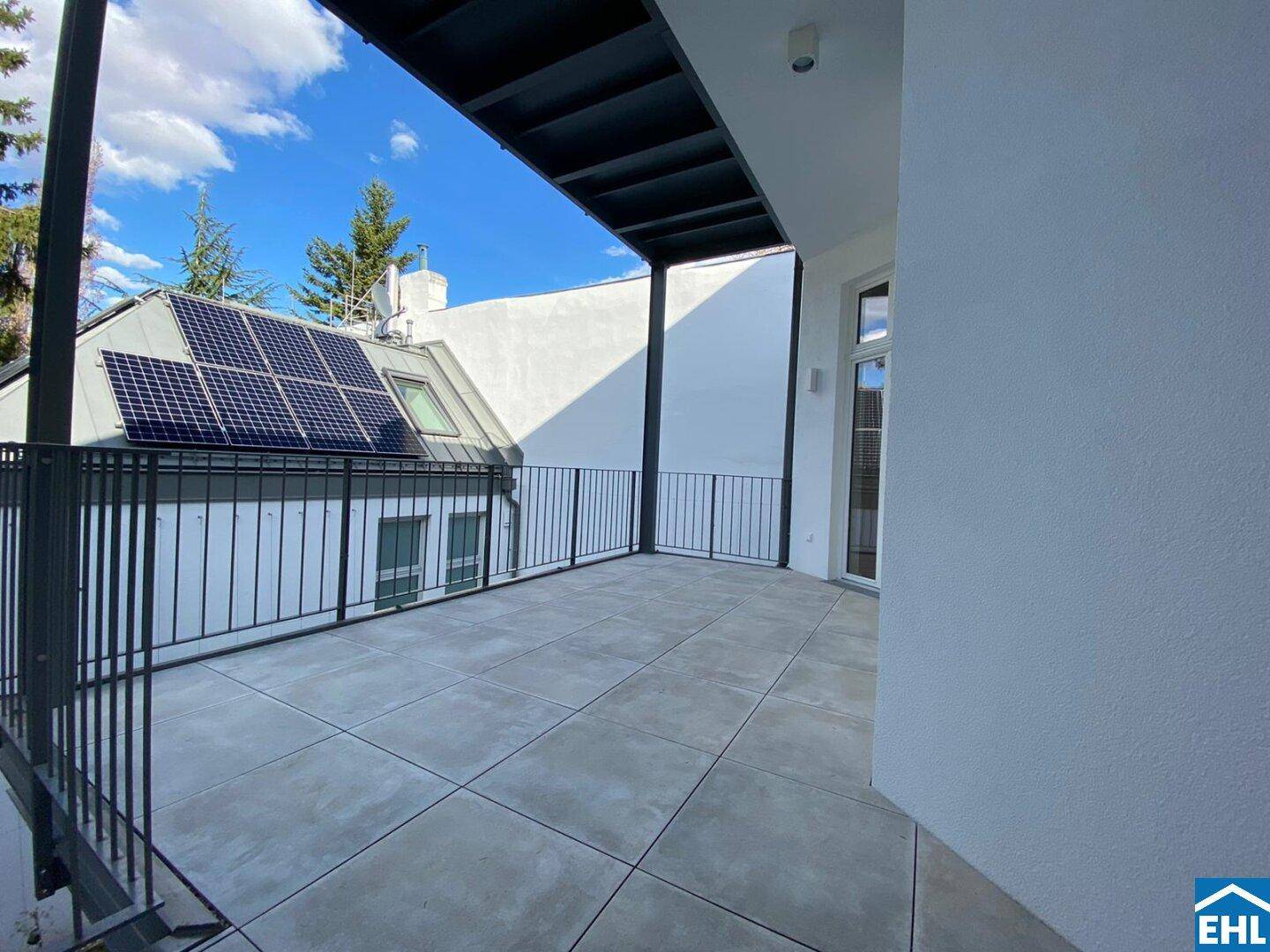 Geräumige Terrasse mit Fliesenboden und Blick auf ein Gebäude mit Solarpaneelen auf dem Dach.