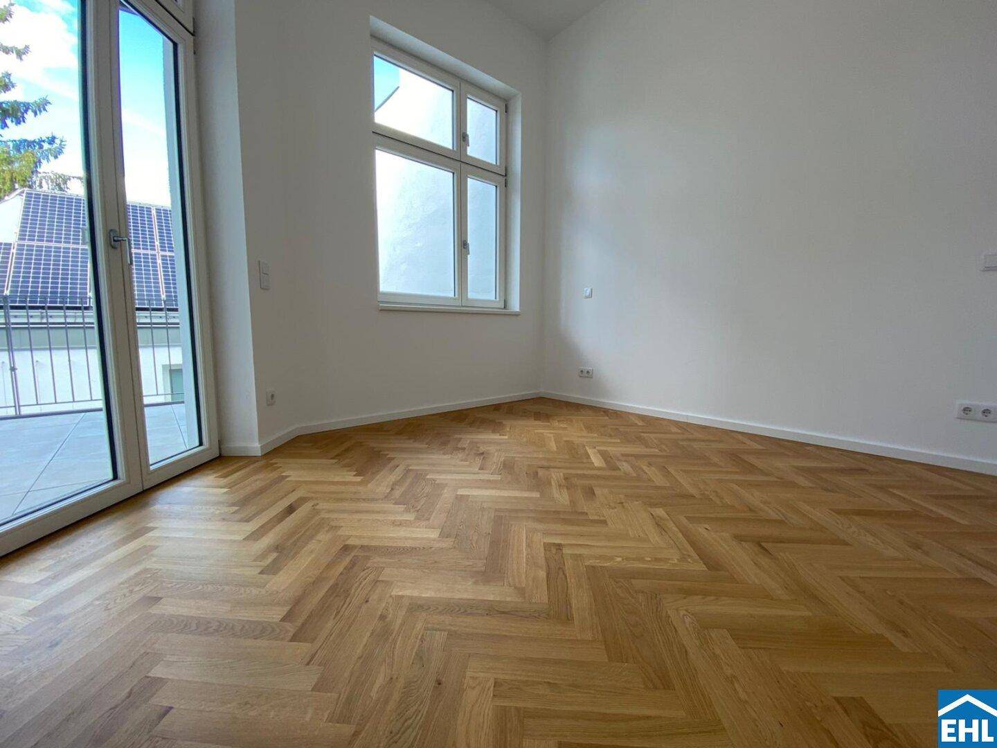 Helles Zimmer mit Fischgrätparkett und Zugang zu einer Terrasse, mit Blick auf Solarpaneele.