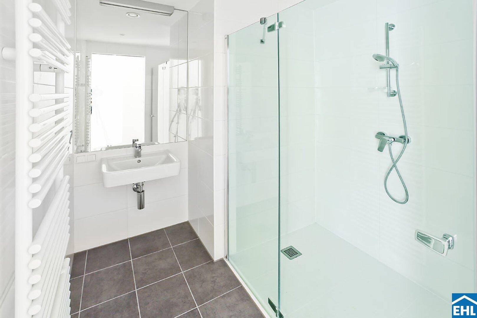 Modernes Badezimmer mit ebenerdiger Dusche, weißen Fliesen und beheiztem Handtuchhalter.