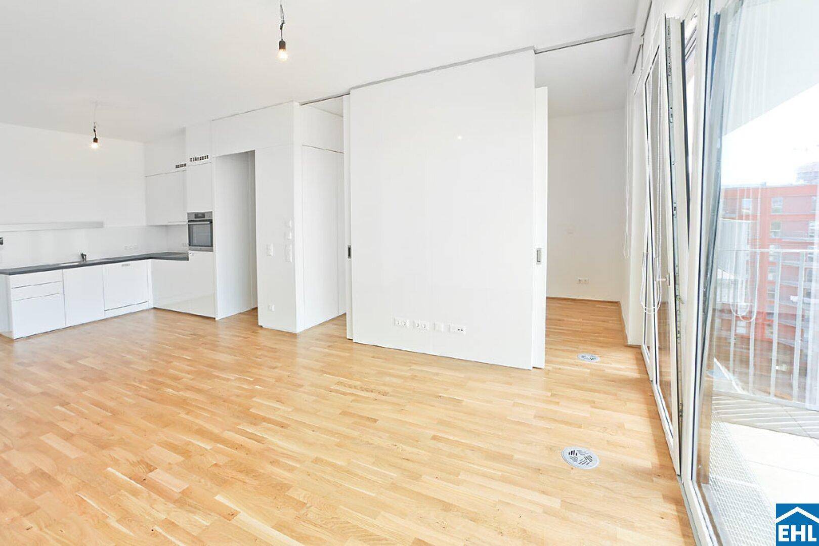 Offener Wohnbereich mit integrierter Küche und direktem Zugang zu einem hellen Balkon.