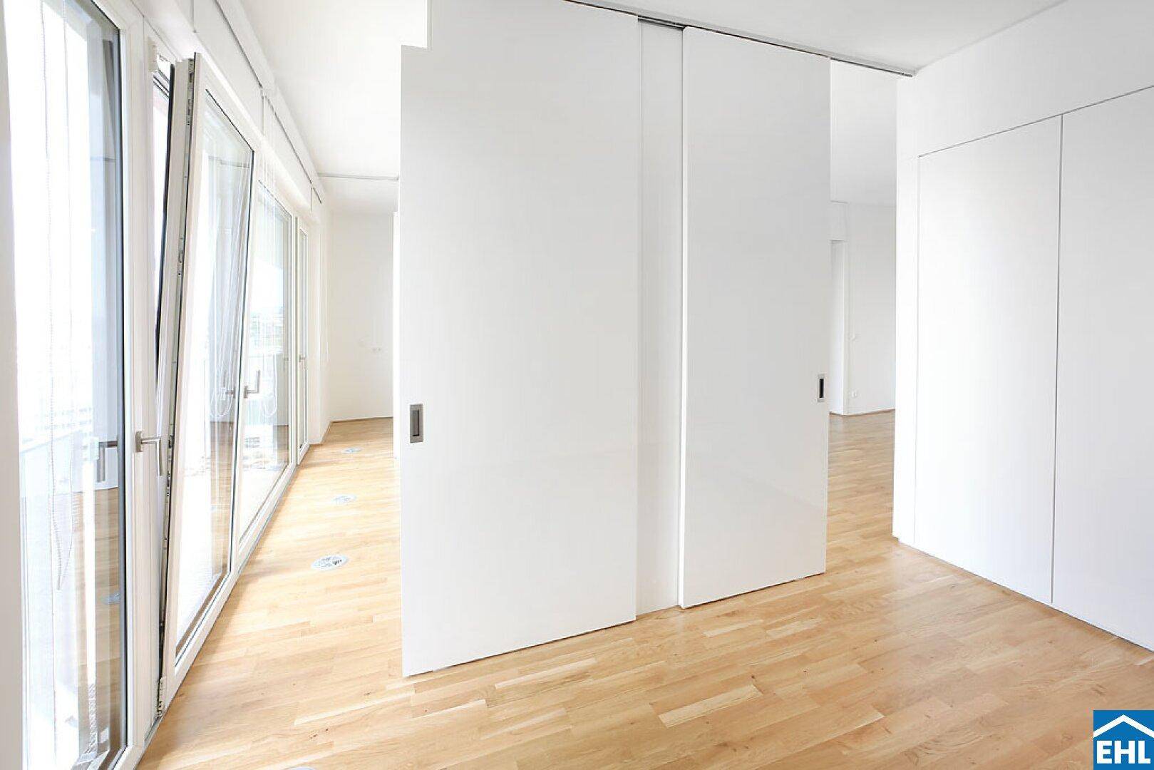 Heller Flur mit Schiebetüren und Holzboden, der zu den Wohnbereichen führt.