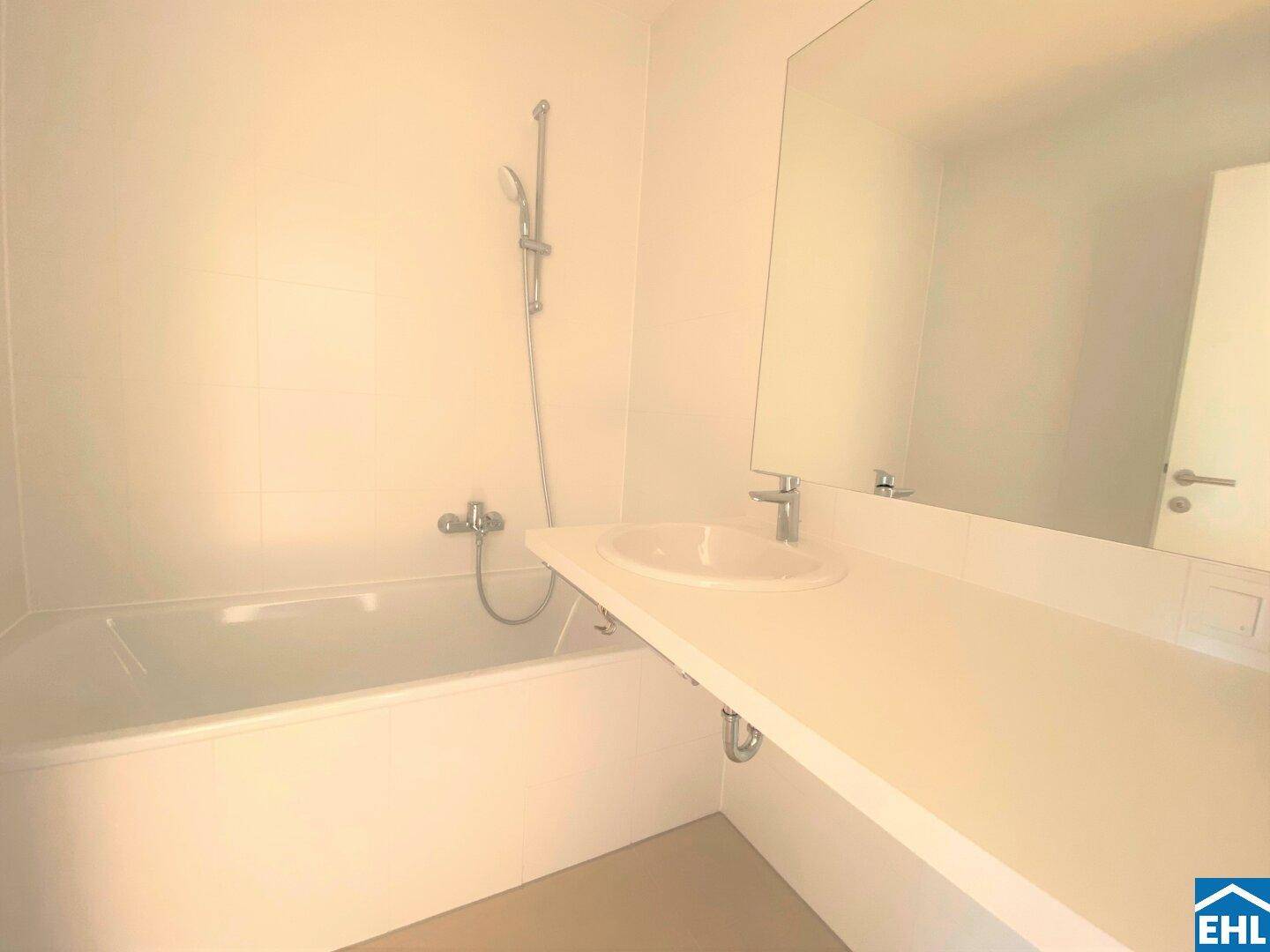 Modernes Badezimmer mit Badewanne, Einzelwaschbecken und großem Spiegel, hell gefliest.
