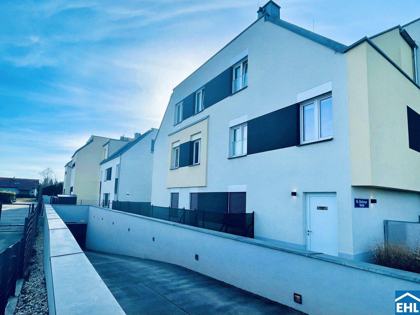Ansicht der modernen Wohnanlage mit Zufahrt zur Tiefgarage und heller Fassade bei Sonnenschein.