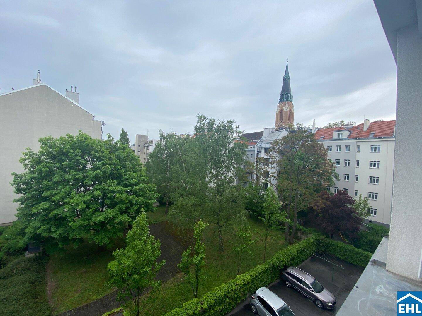 Blick auf einen grünen Innenhof mit Bäumen und einer Kirche im Hintergrund, von einem oberen Stockwerk.