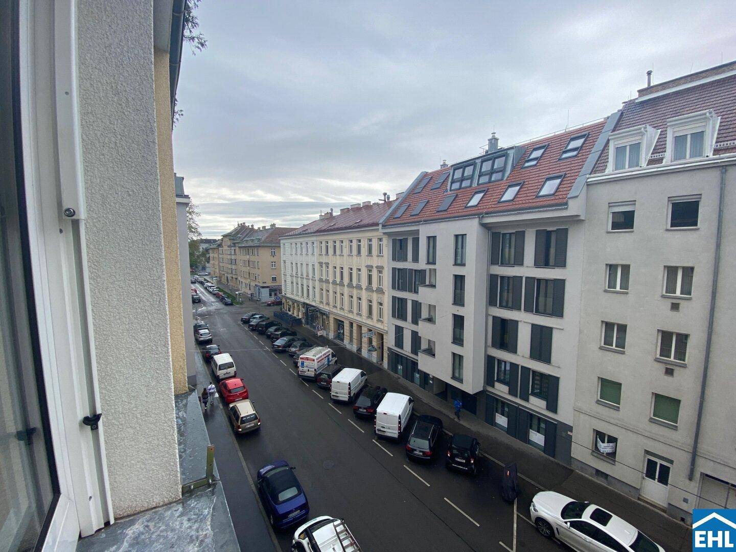 Blick von oben auf eine belebte Stadtstraße mit parkenden Autos und angrenzenden Gebäuden.
