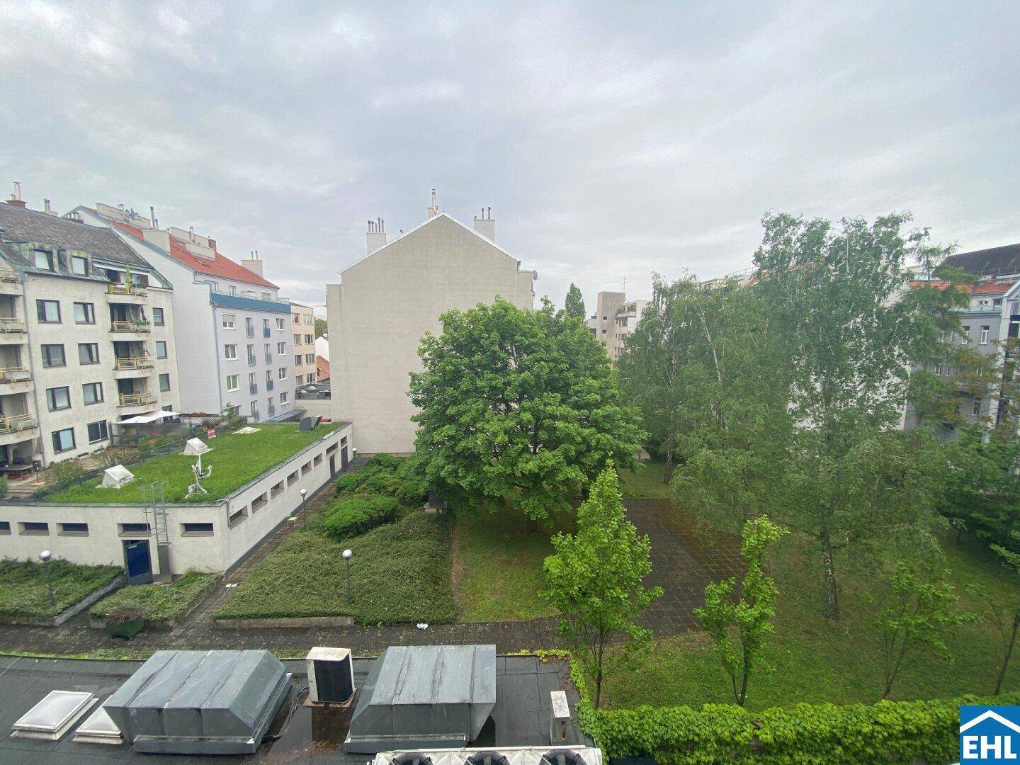 Weitläufiger Blick auf einen begrünten Innenhof mit verschiedenen Bäumen und Gebäuden.