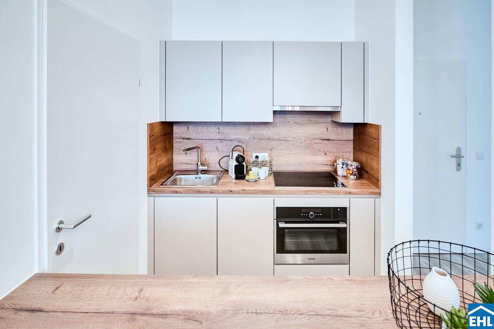 Kompakte Einbauküche mit modernen Geräten, Spüle und Holzrückwand.
