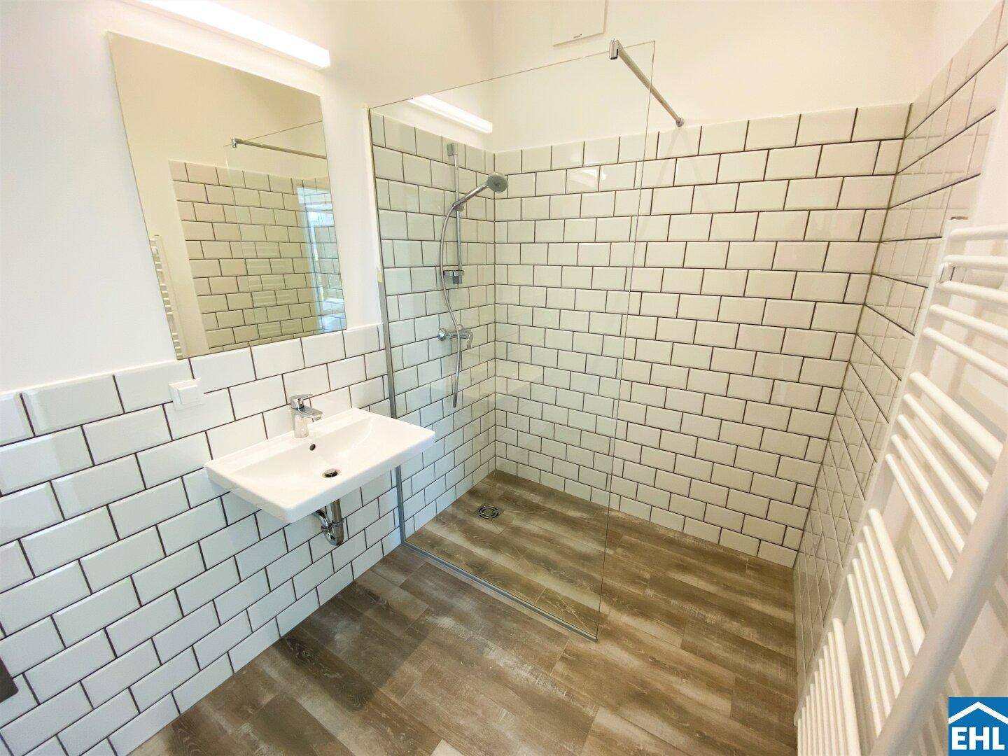 Modernes Badezimmer mit ebenerdiger Dusche, weißen Fliesen und Einzelwaschbecken.