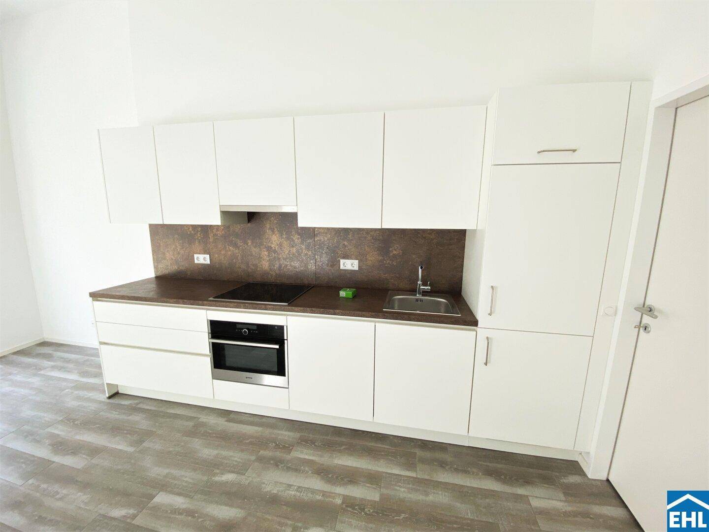 Moderne Einbauküche in Weiß mit integrierten Geräten und dunkler Arbeitsplatte.