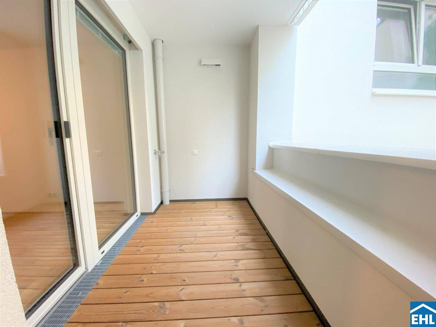 Schmaler Balkon mit Holzdielen und großer Glasschiebetür, die viel Licht hereinlässt.