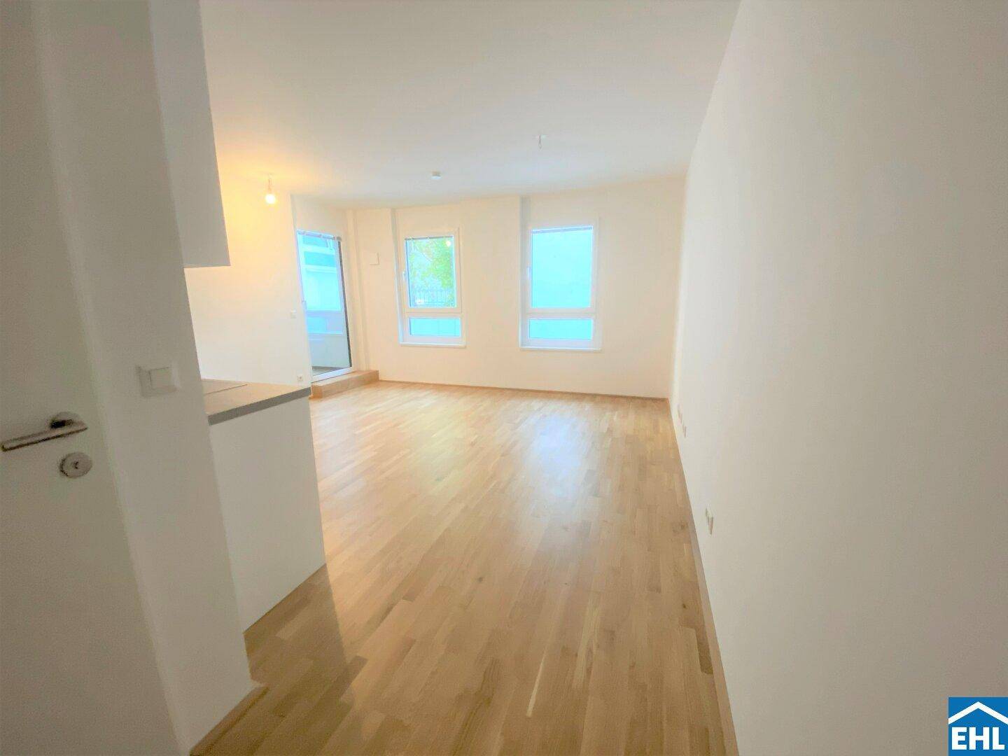Lichtdurchfluteter Wohnbereich mit großen Fenstern und hellem Parkettboden, ideal für modernes Wohnen.
