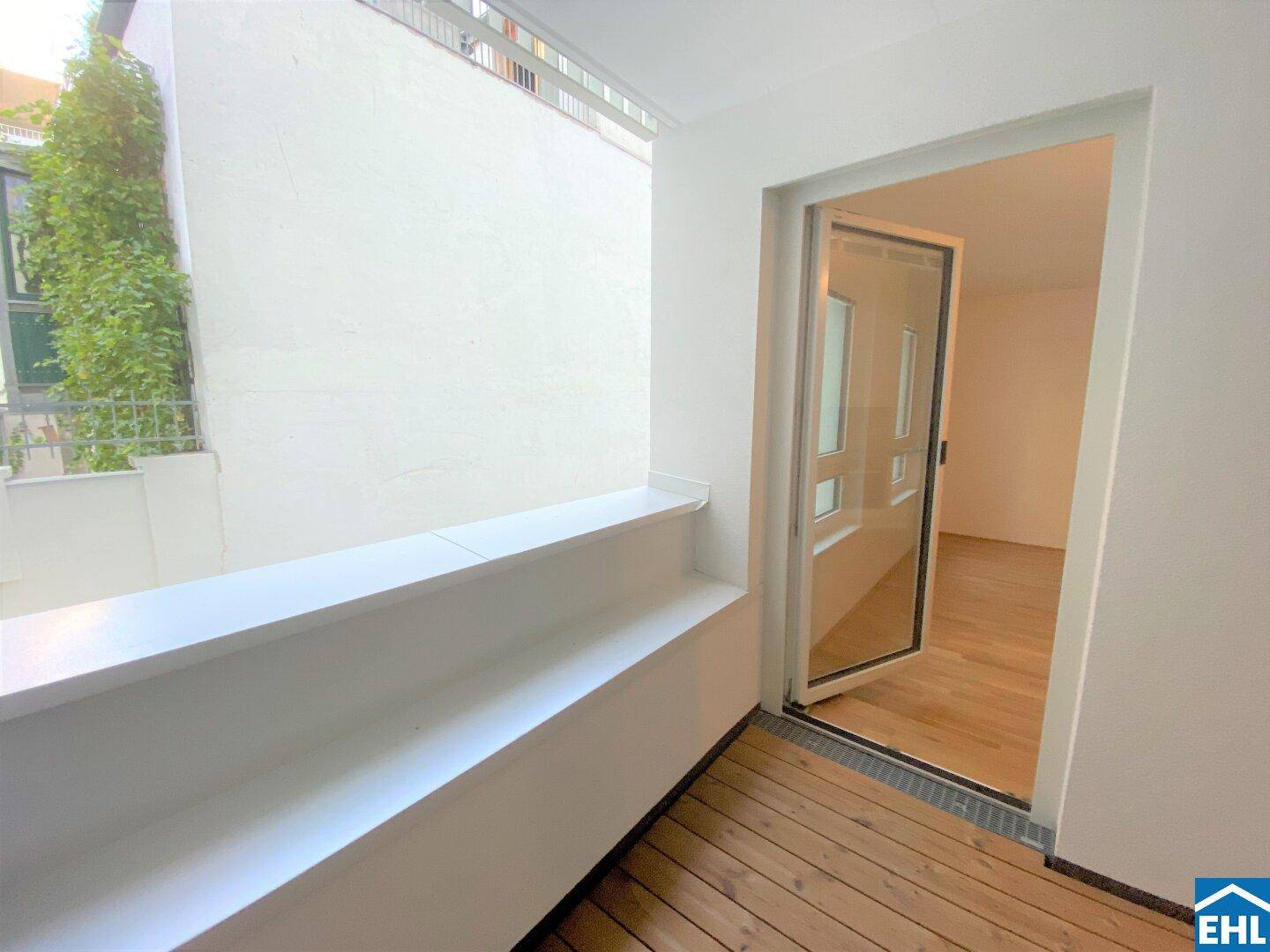 Kleiner, überdachter Balkon mit Holzboden und Blick auf eine begrünte Wand.