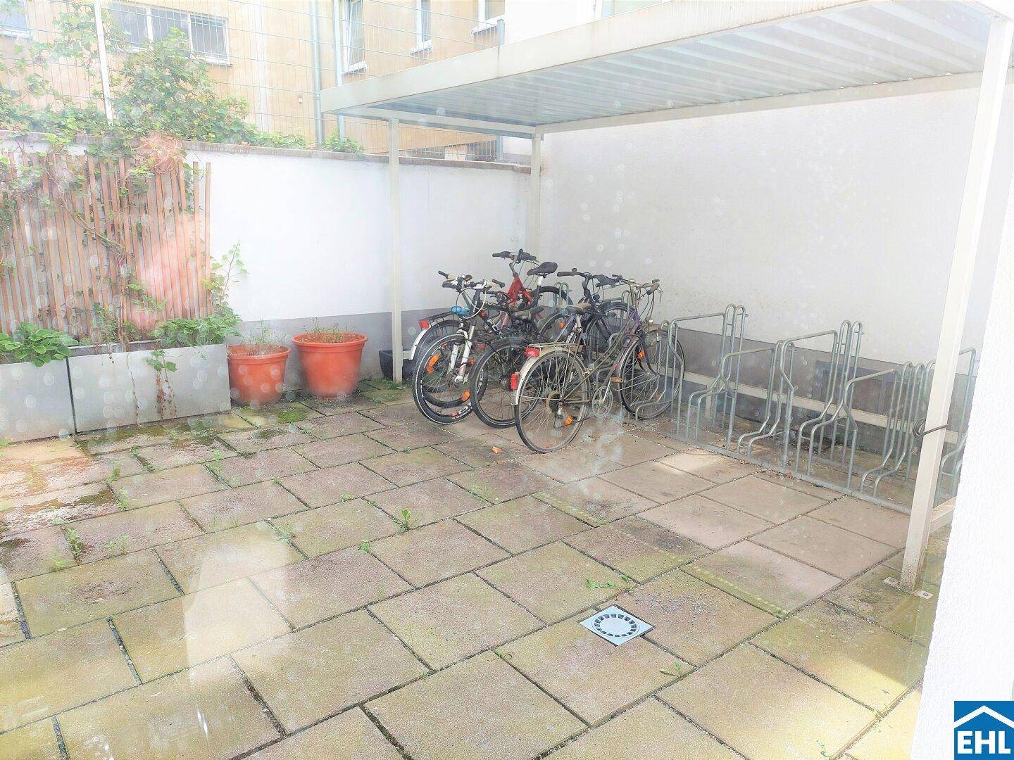 Überdachter Fahrradabstellplatz im Außenbereich mit Steinplattenboden und Pflanzen.
