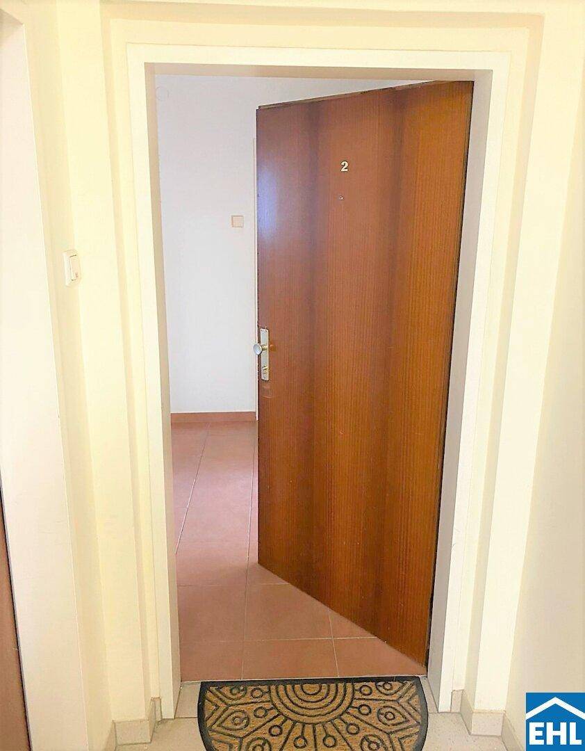 Eingangsbereich mit Holztür und Fliesenboden, der zu den Wohnräumen führt.