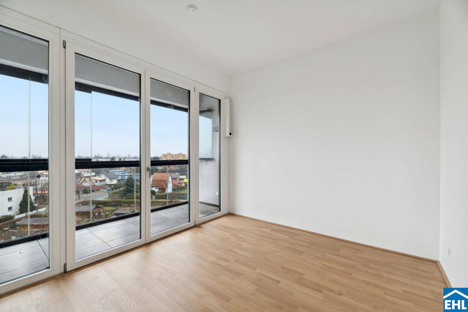 Heller Wohnraum mit großen Fenstern, die Zugang zu einem Balkon bieten und einen weiten Blick ermöglichen.