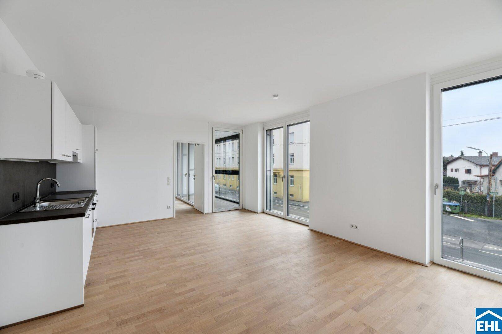 Lichtdurchfluteter Wohnbereich mit offener Küche, Parkett und großen Fenstern zur Straße.
