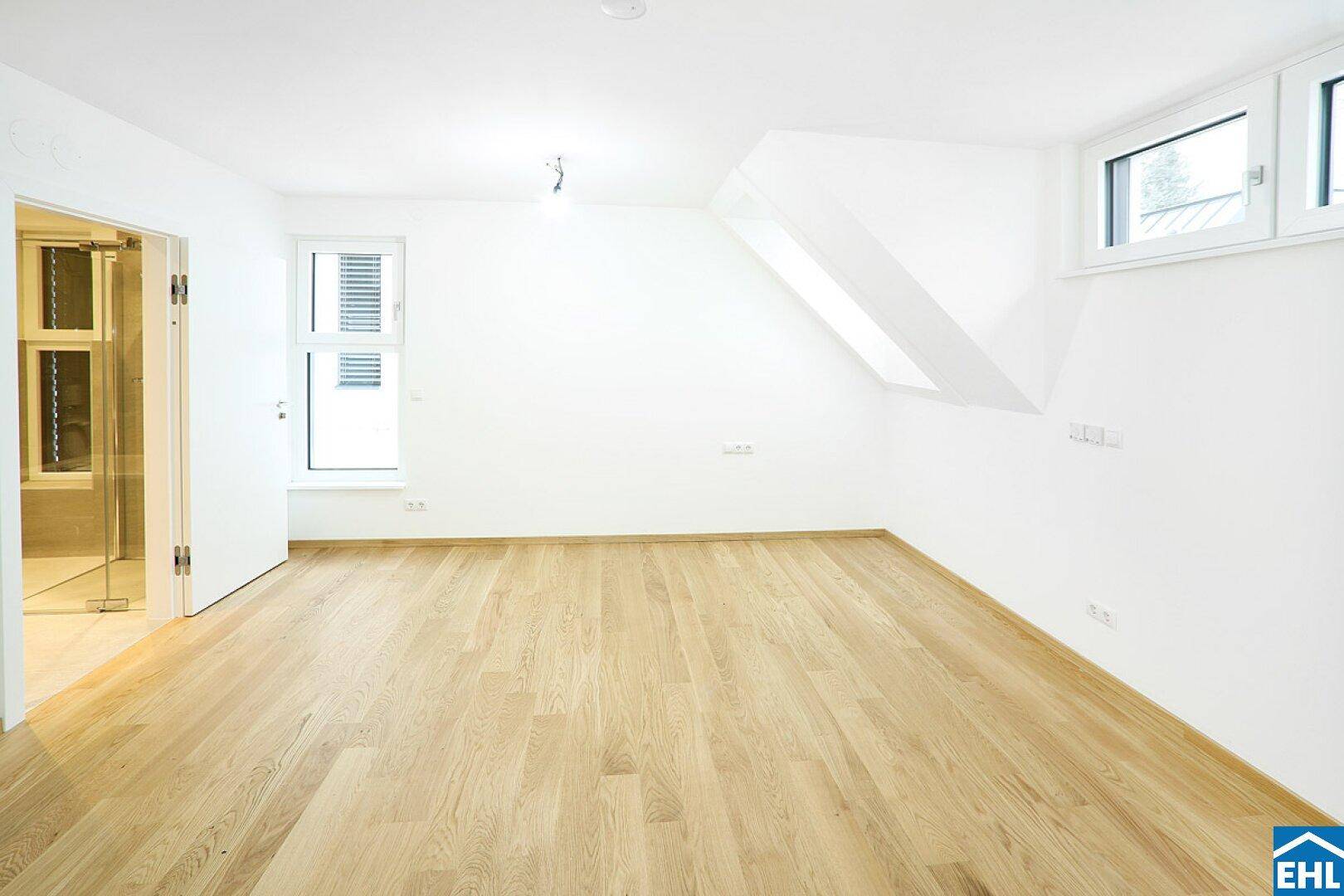 Helles Schlafzimmer mit Holzboden, Dachschrägen und Zugang zu einem modernen Badezimmer.
