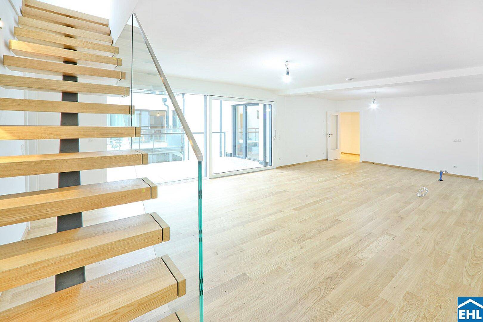 Heller Wohnbereich mit hochwertigem Parkettboden, moderner Treppe und viel Tageslicht.