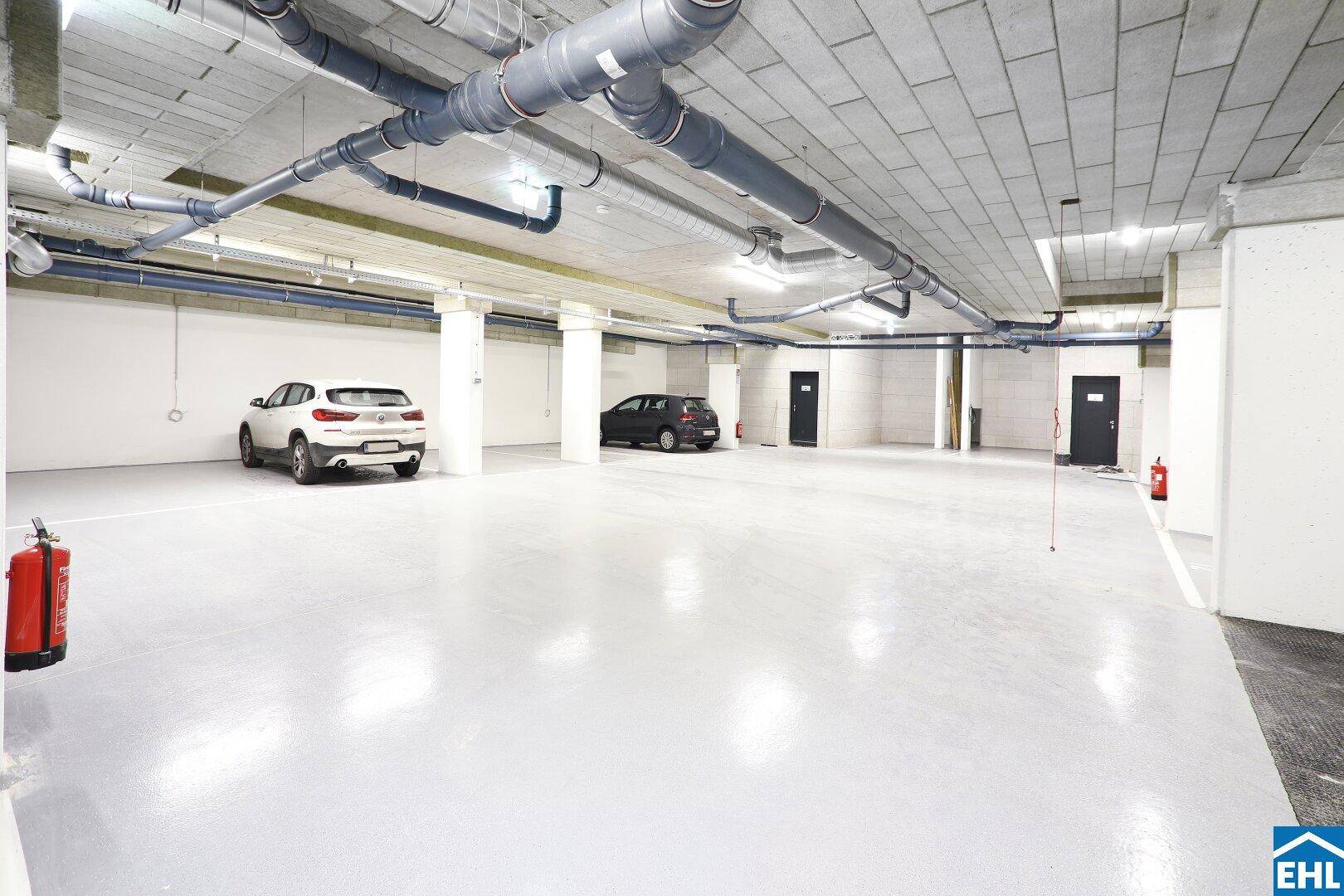 Geräumige Tiefgarage mit mehreren Stellplätzen und sichtbaren Versorgungsleitungen an der Decke.