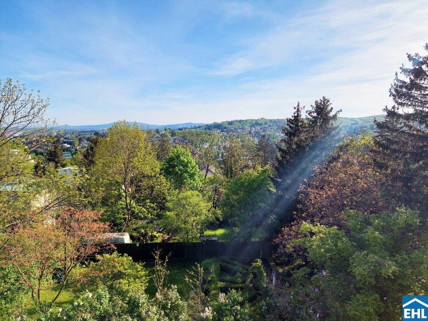 Weitläufiger grüner Ausblick über Bäume und Hügel mit Fernsicht auf die Stadt.
