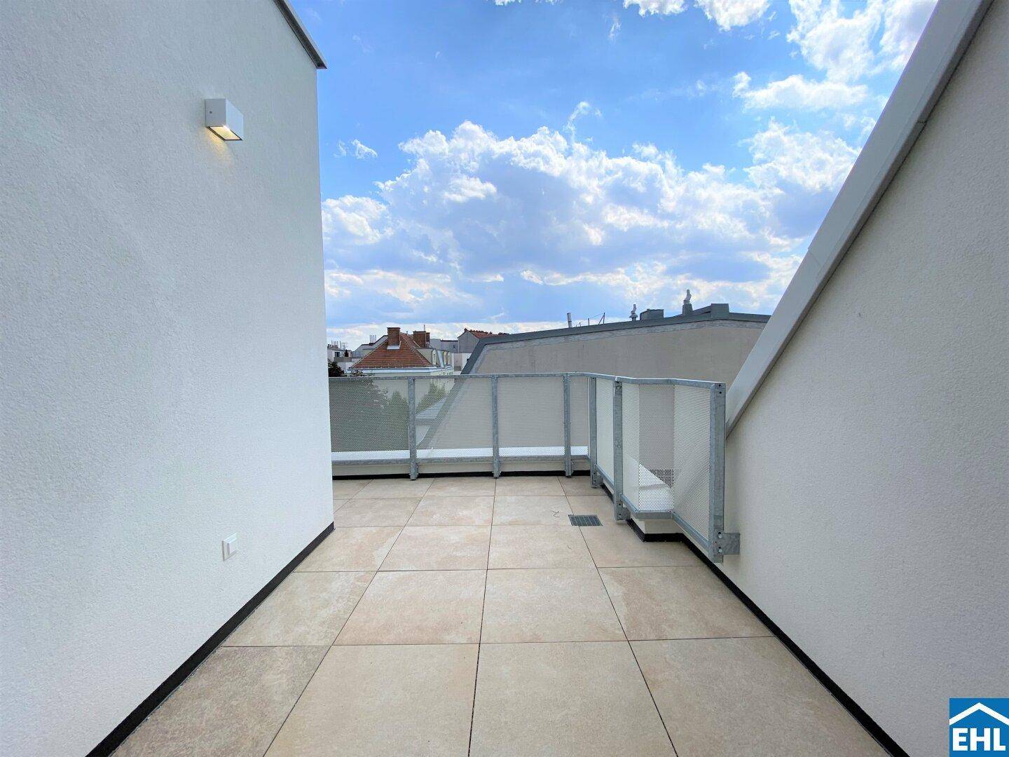 Geräumige Dachterrasse mit Fliesenboden und Blick auf die umliegenden Gebäude und den Himmel.