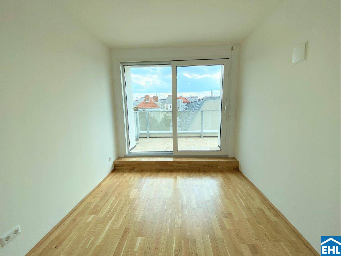 Helles Zimmer mit Parkettboden und Zugang zu einem Außenbereich durch große Schiebetüren.