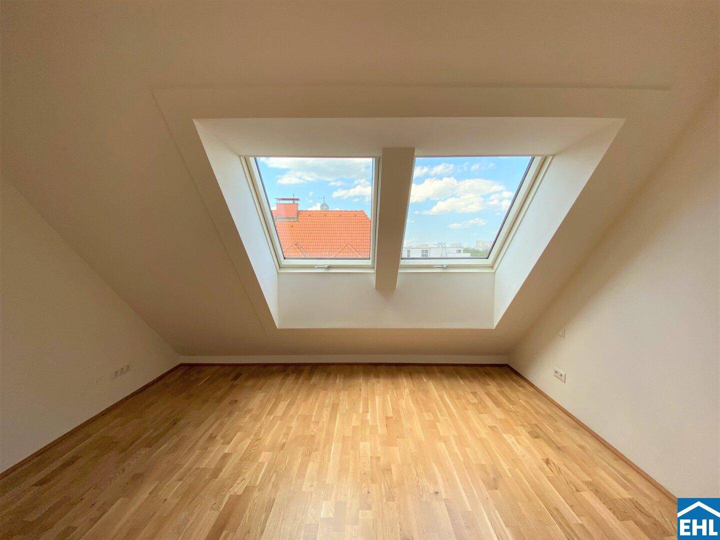 Dachzimmer mit Holzboden und zwei großen Dachfenstern, die viel natürliches Licht hereinlassen.