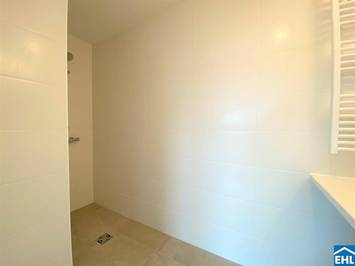 Helles Badezimmer mit ebenerdiger Dusche, weißen Fliesen und beheiztem Handtuchhalter.