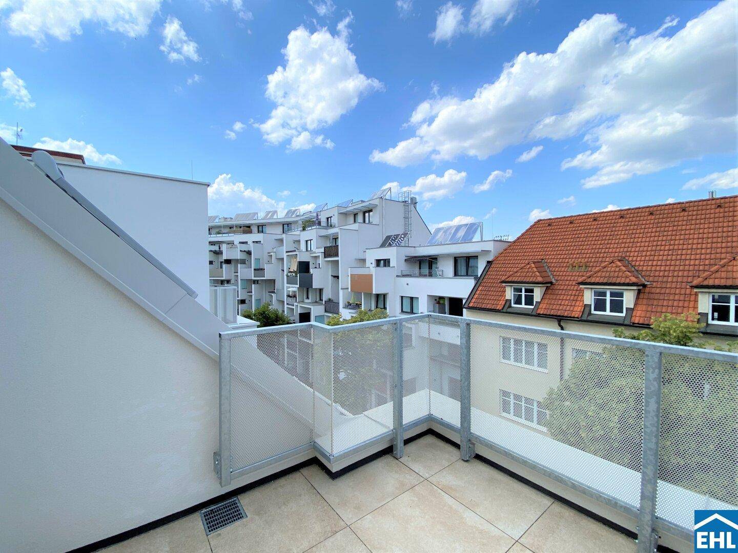 Sonniger Außenbereich mit Fliesenboden und Blick auf die Dächer der Stadt und die Umgebung.