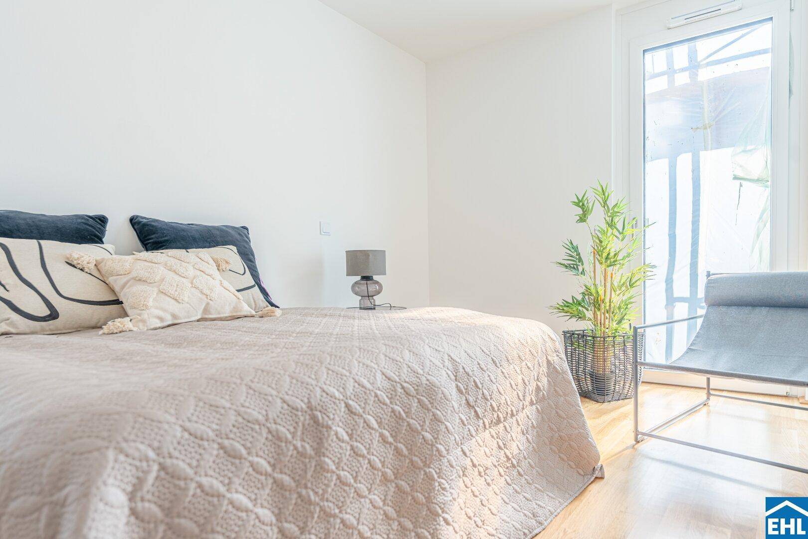 Helles Schlafzimmer mit Doppelbett, Nachttisch und Zugang zu einem Balkon oder einer Terrasse.