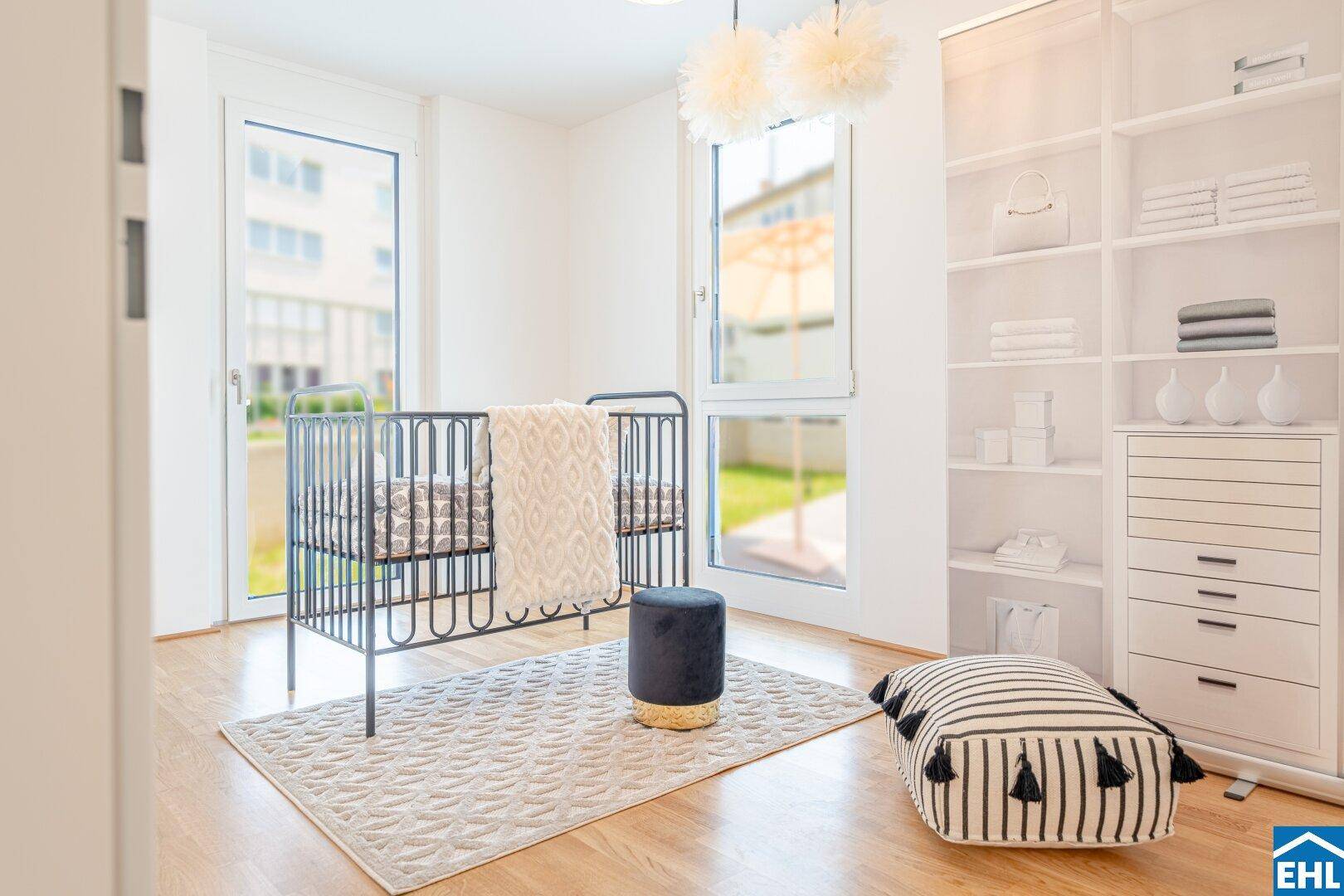 Freundliches Kinderzimmer mit Gitterbett, offenem Regal und viel Tageslicht durch große Fenster.