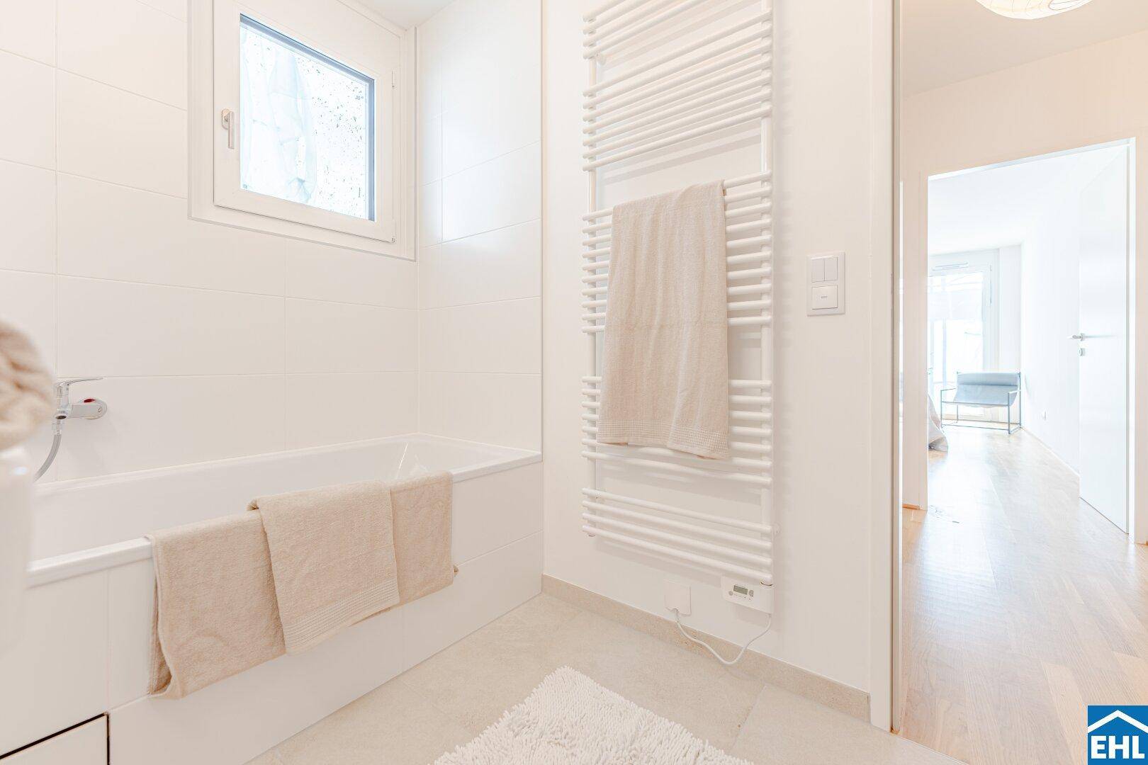 Helles Badezimmer mit Badewanne, beheiztem Handtuchhalter und einem Fenster.